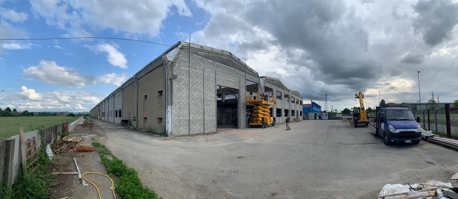 Area industriale adibita a magazzino con edifici in cemento, veicoli parcheggiati e cielo nuvoloso.