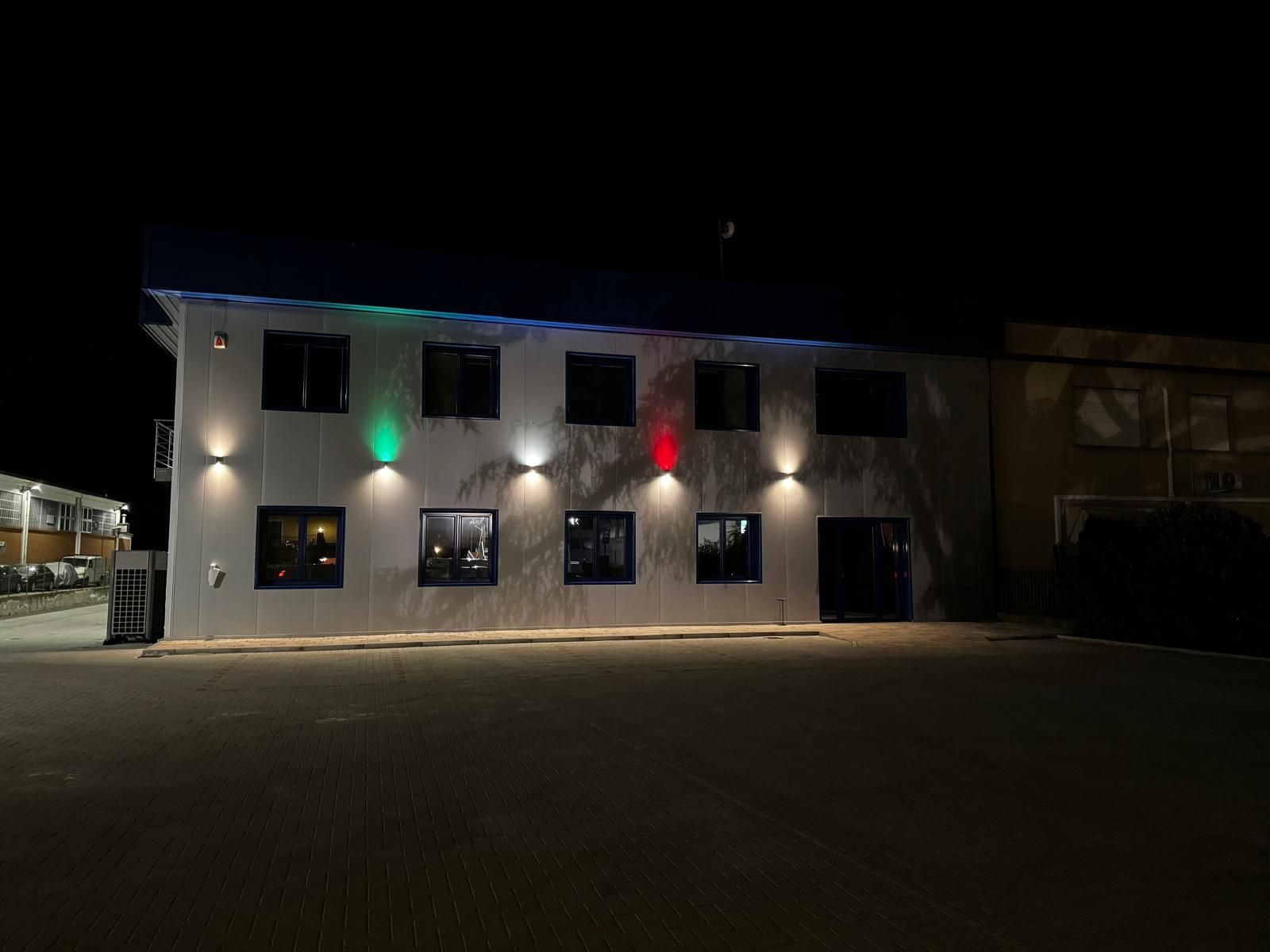 Esterno notturno di un edificio con finestre illuminate e luci rosse e verdi sopra l'ingresso.