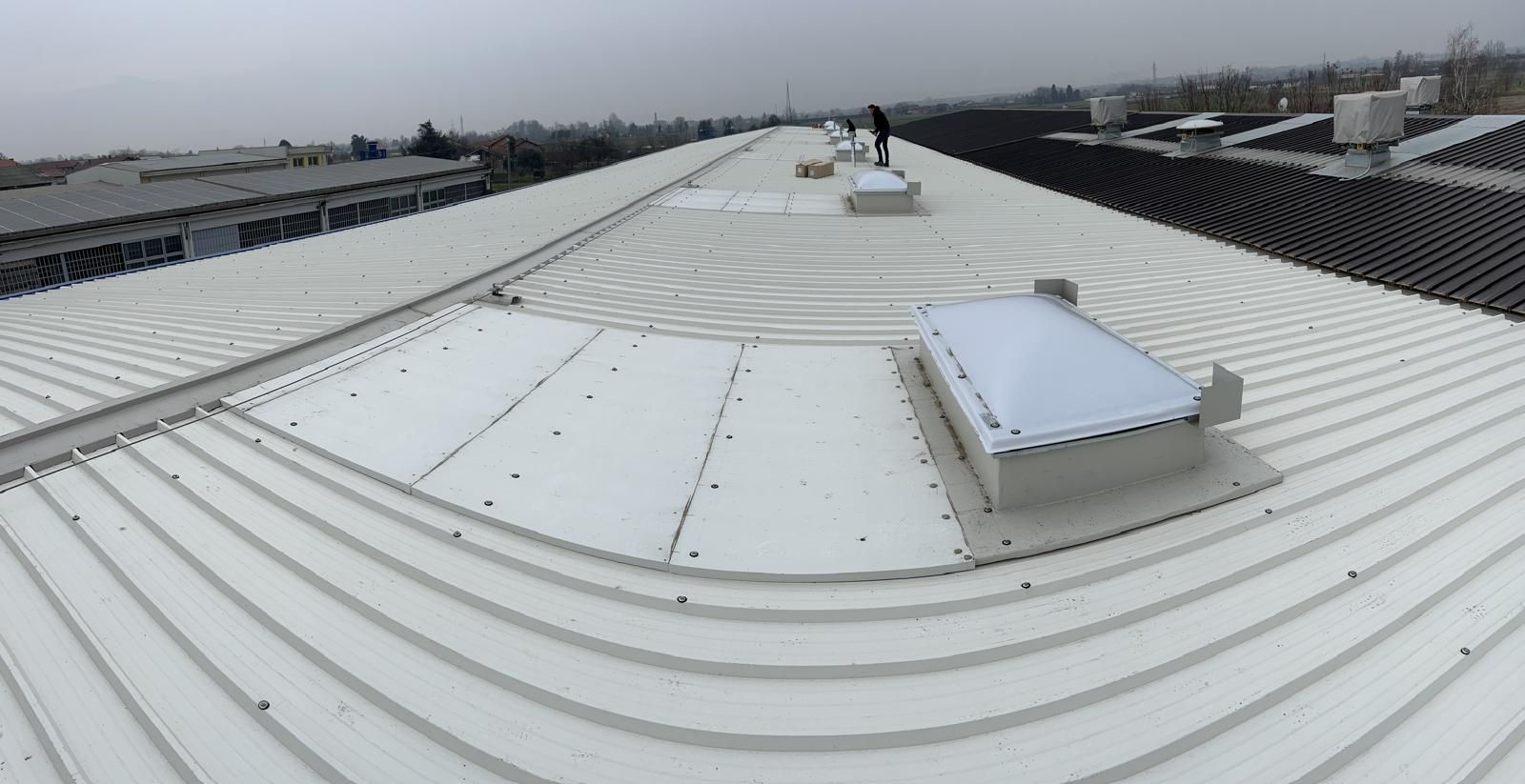 Tetto in metallo bianco con creste curve e due lucernari sotto un cielo nuvoloso.