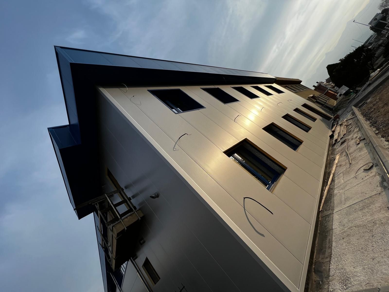 Edificio moderno inclinato con facciata bianca e finestre scure sullo sfondo di un cielo nuvoloso.