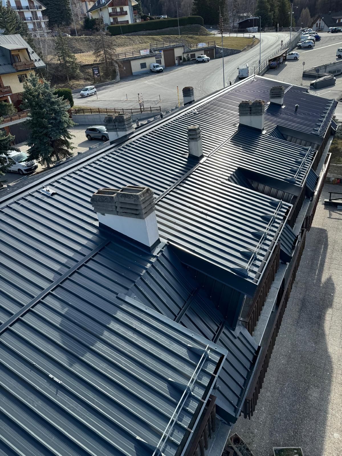 Tetto in metallo di un lungo edificio con camini, visto dall'alto a lato di una strada.