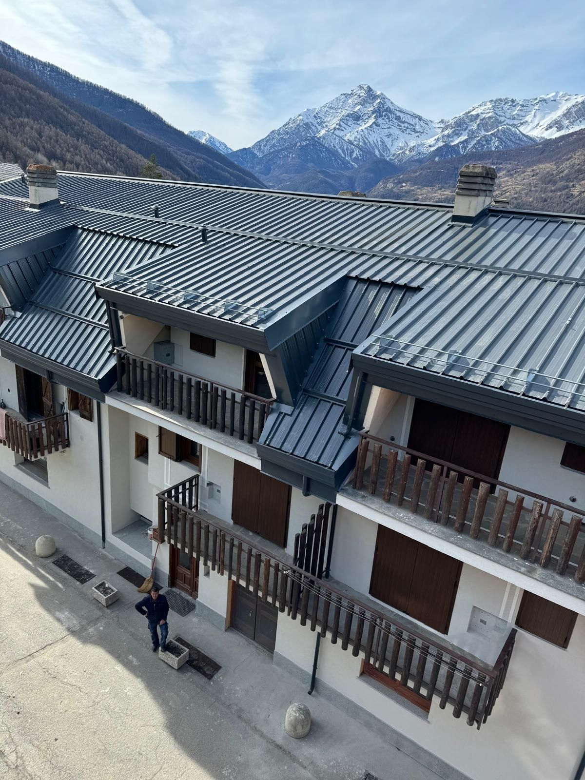 Rifugio di montagna con tetto grigio scuro, balconi in legno e cime innevate sullo sfondo.