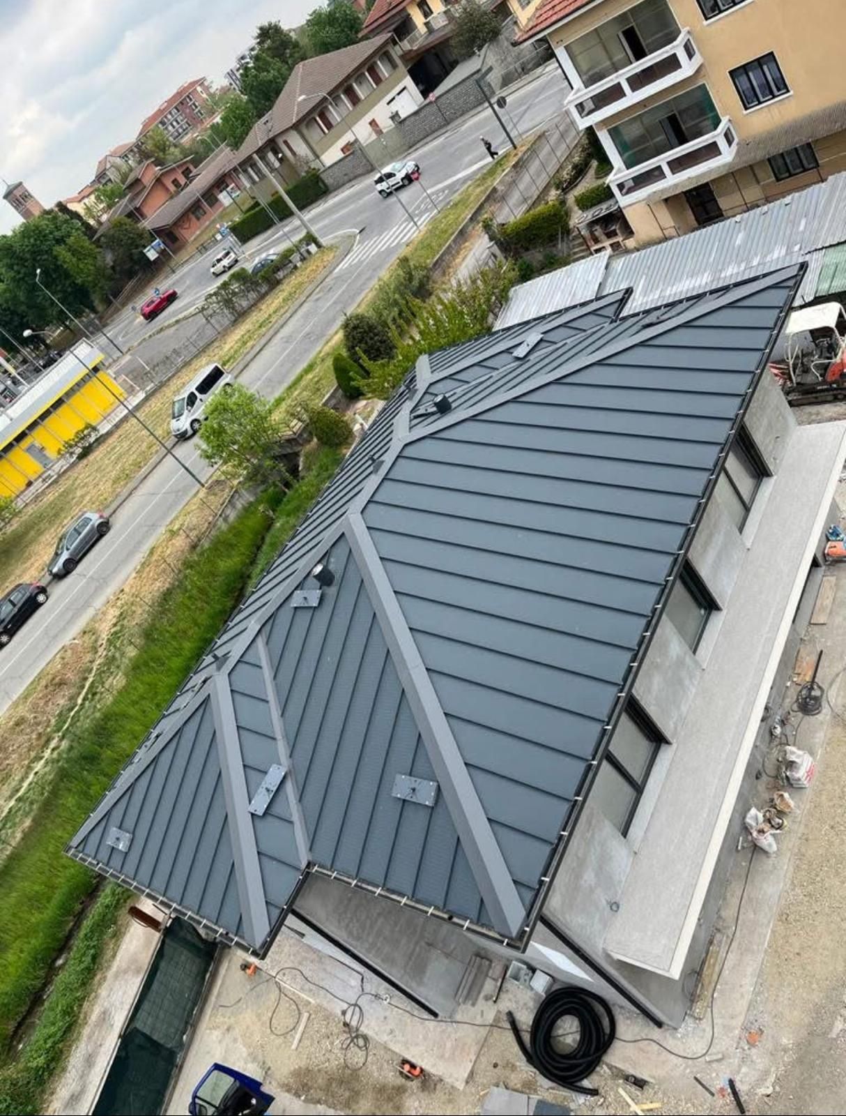 Veduta aerea di una piccola casa con tetto in metallo grigio scuro in un quartiere residenziale.