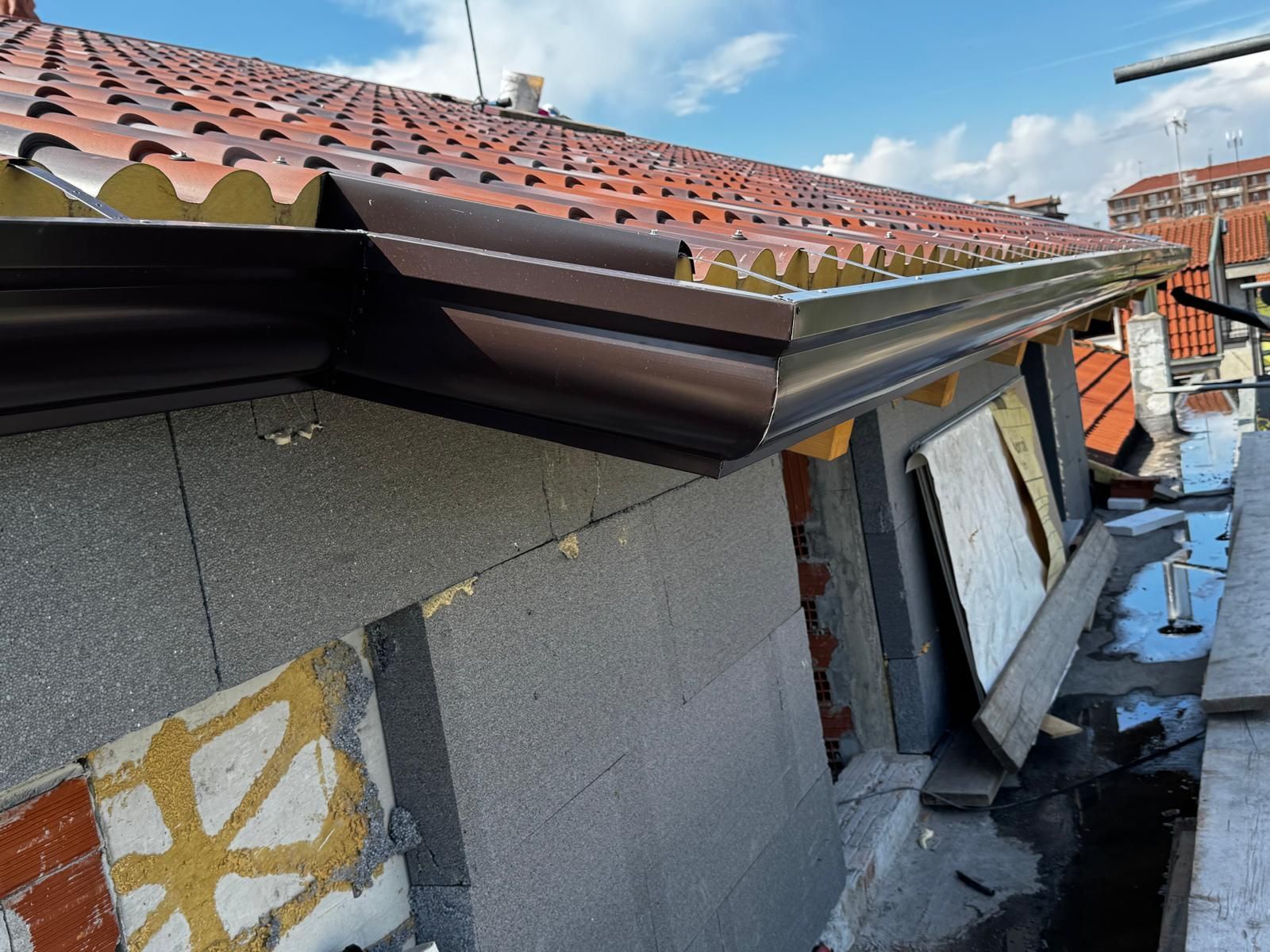 Tetto con grondaia metallica danneggiata e bordo del tetto a vista accanto a muri grigi dell'edificio.