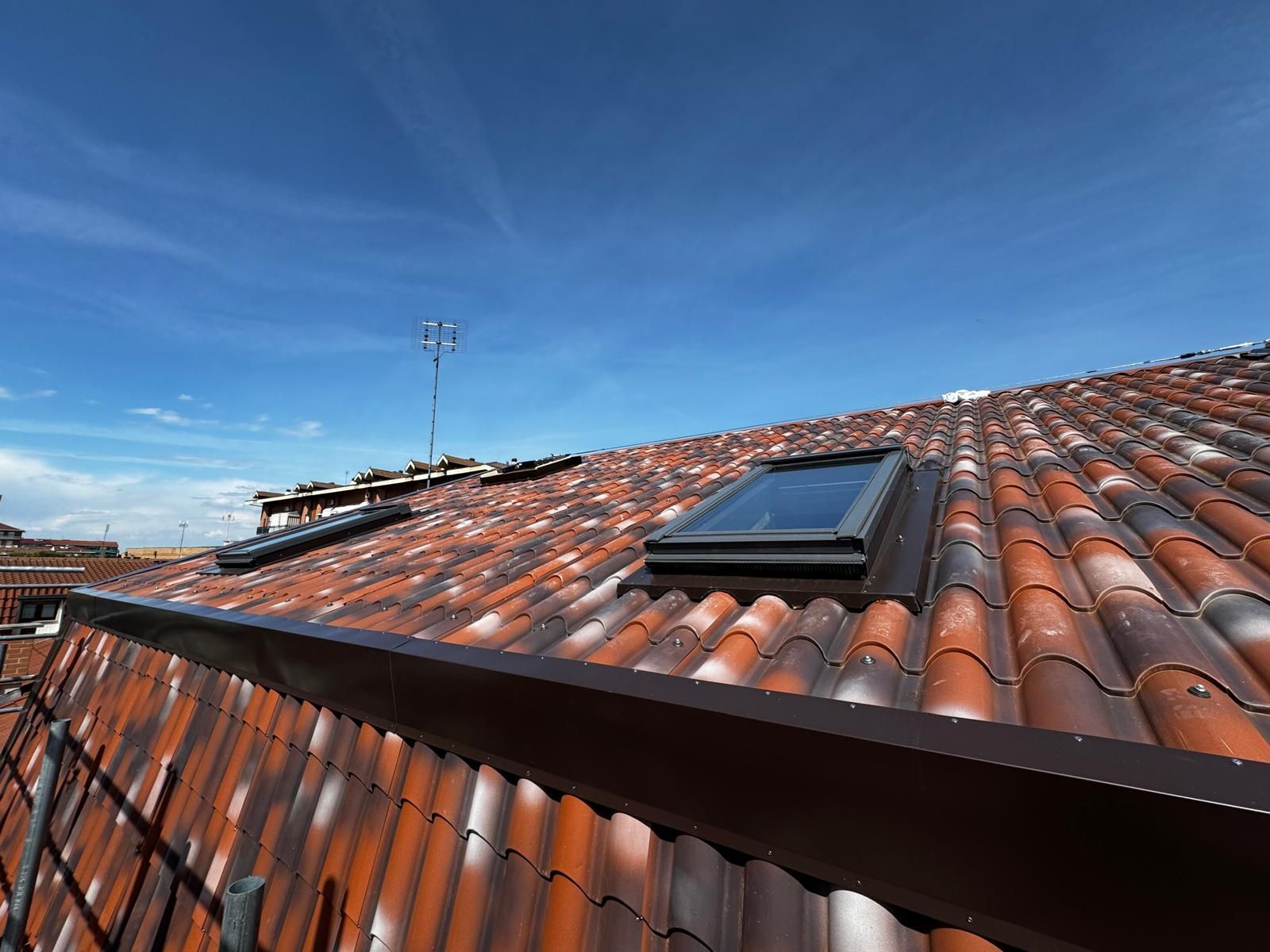 Tetto con tegole rosse, lucernario e antenna sotto un cielo azzurro limpido.