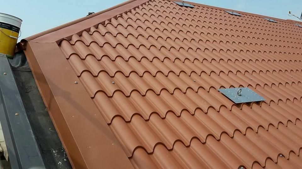 Tetto in tegole di terracotta con piccola botola e bordo della grondaia sotto un cielo limpido