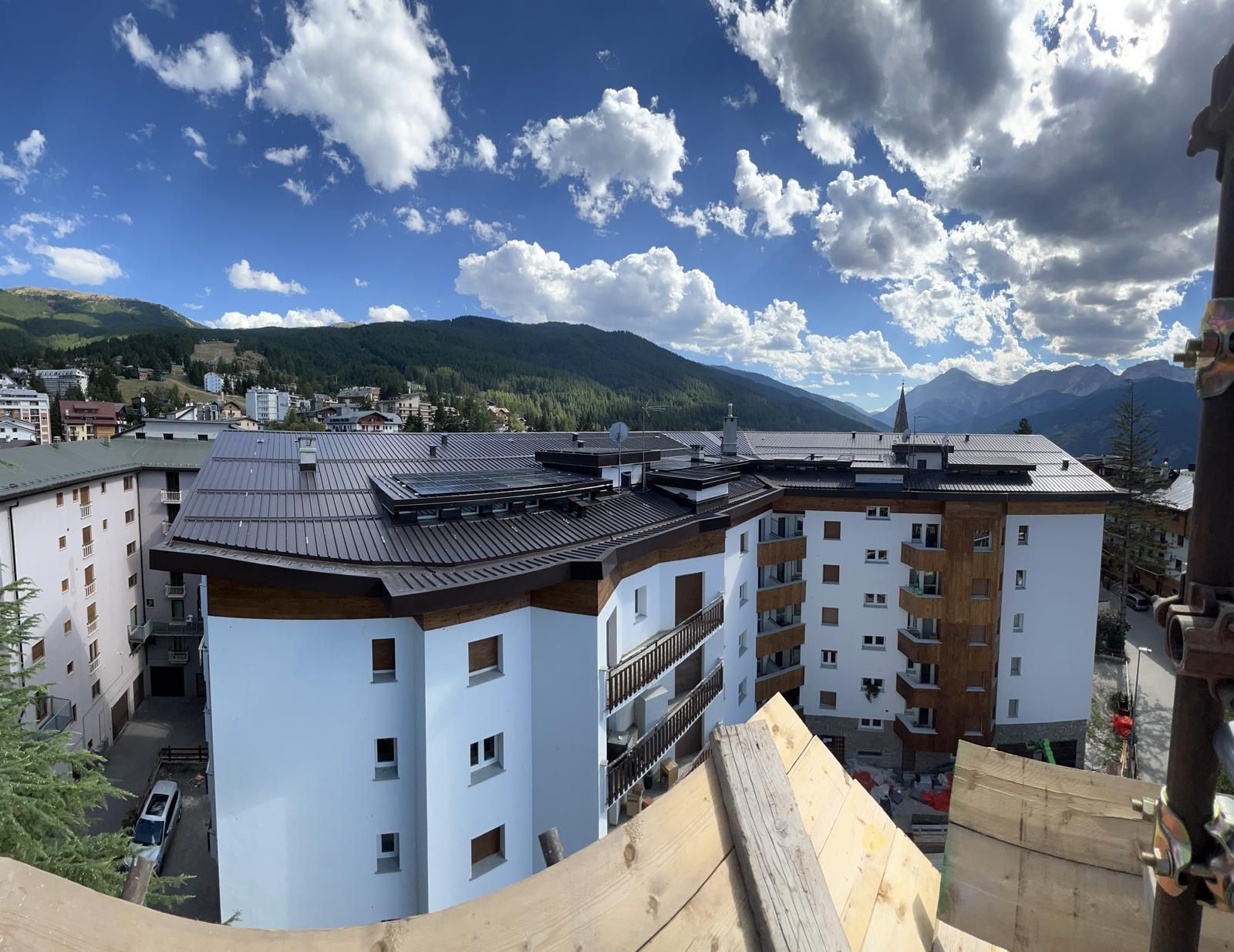 Palazzi di appartamenti in una cittadina di montagna, sotto un cielo azzurro nuvoloso, visti da un balcone sopraelevato.