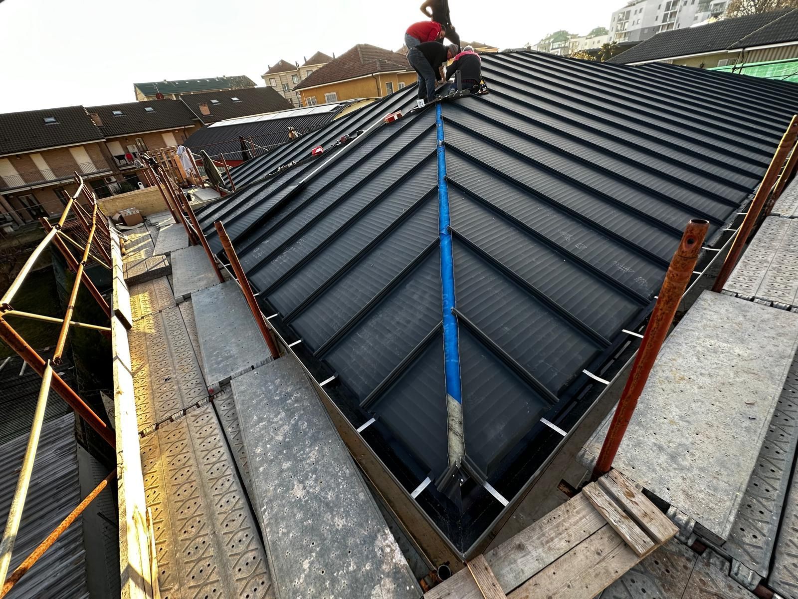 Un operaio su un tetto sta installando pannelli metallici neri accanto a una linea di sicurezza blu.
