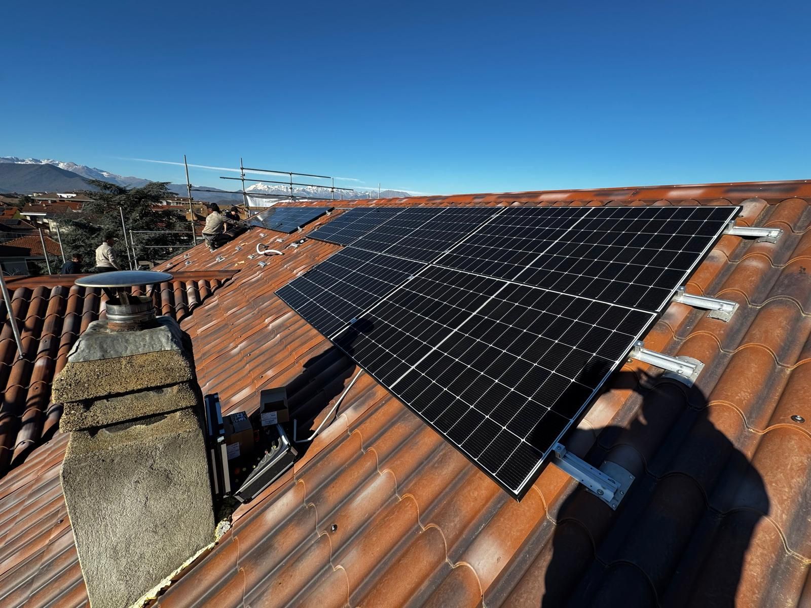 Pannelli solari neri montati su un tetto di tegole di terracotta sotto un cielo azzurro e limpido.