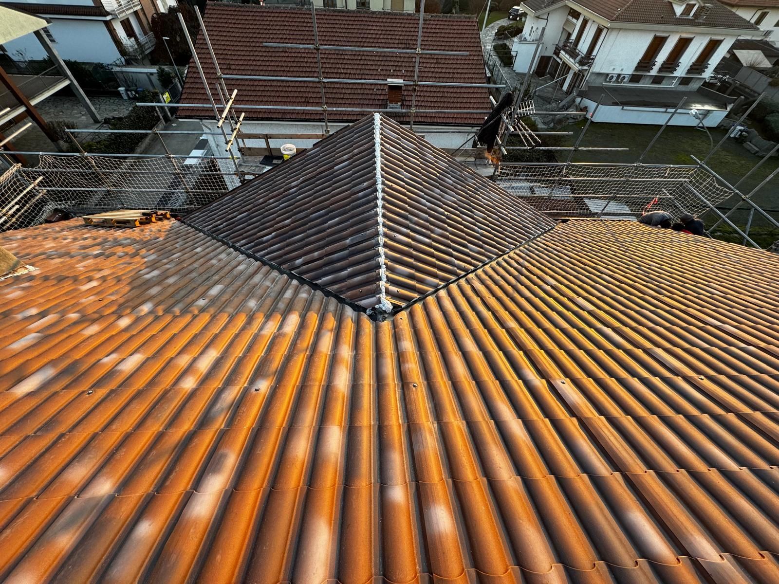 Tetto ondulato arrugginito con una sezione a piramide scura, che si affaccia su edifici e linee elettriche circostanti.