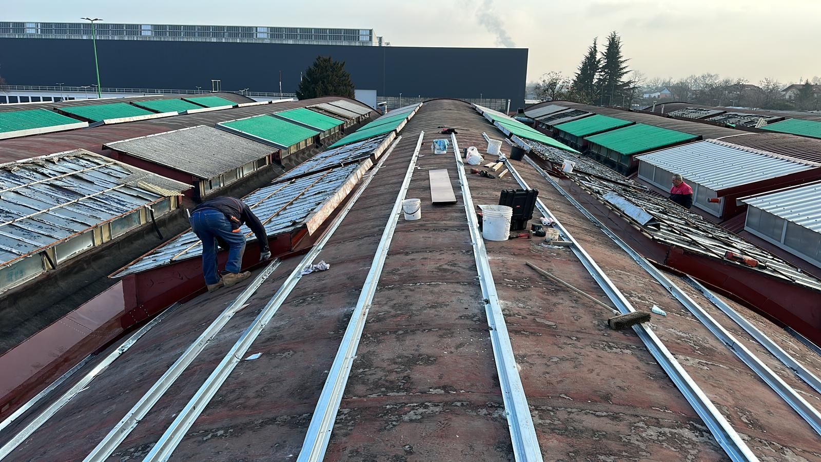 Operai edili installano lunghe strisce metalliche su un tetto inclinato sotto un cielo nuvoloso.