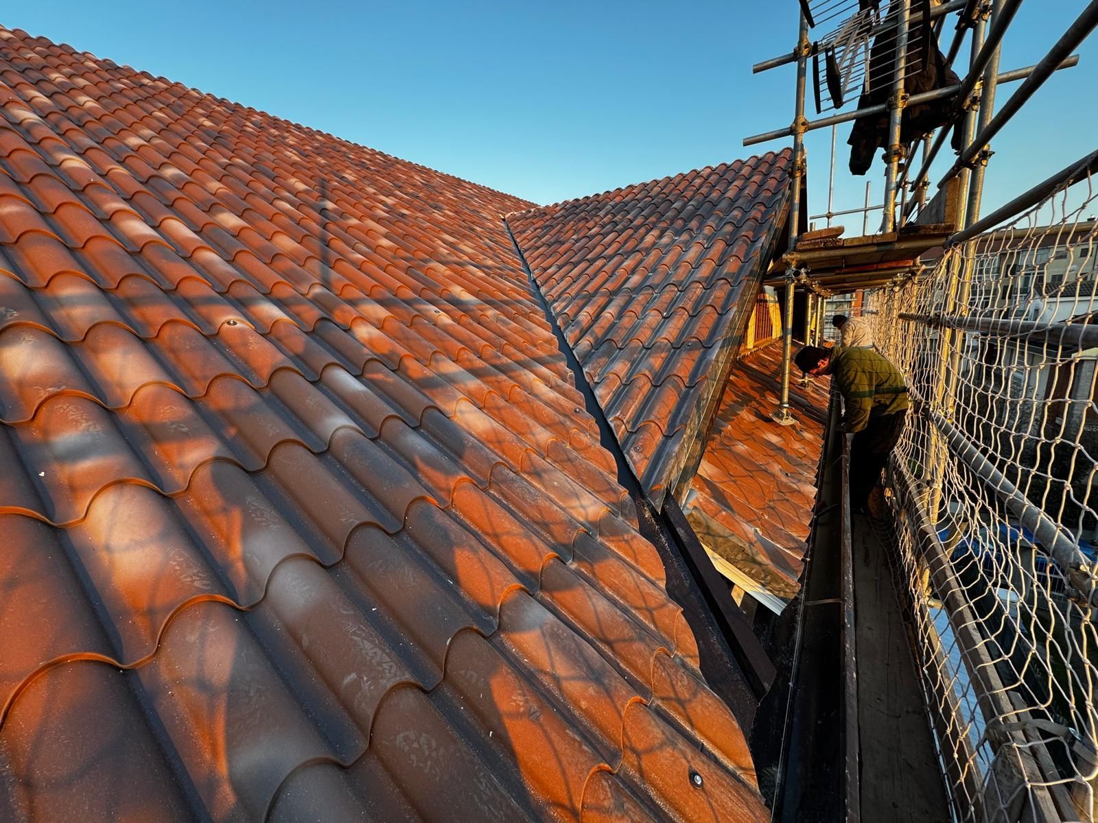 Tetto in riparazione con tegole di terracotta rossa e impalcature accanto a una linea del tetto ripida