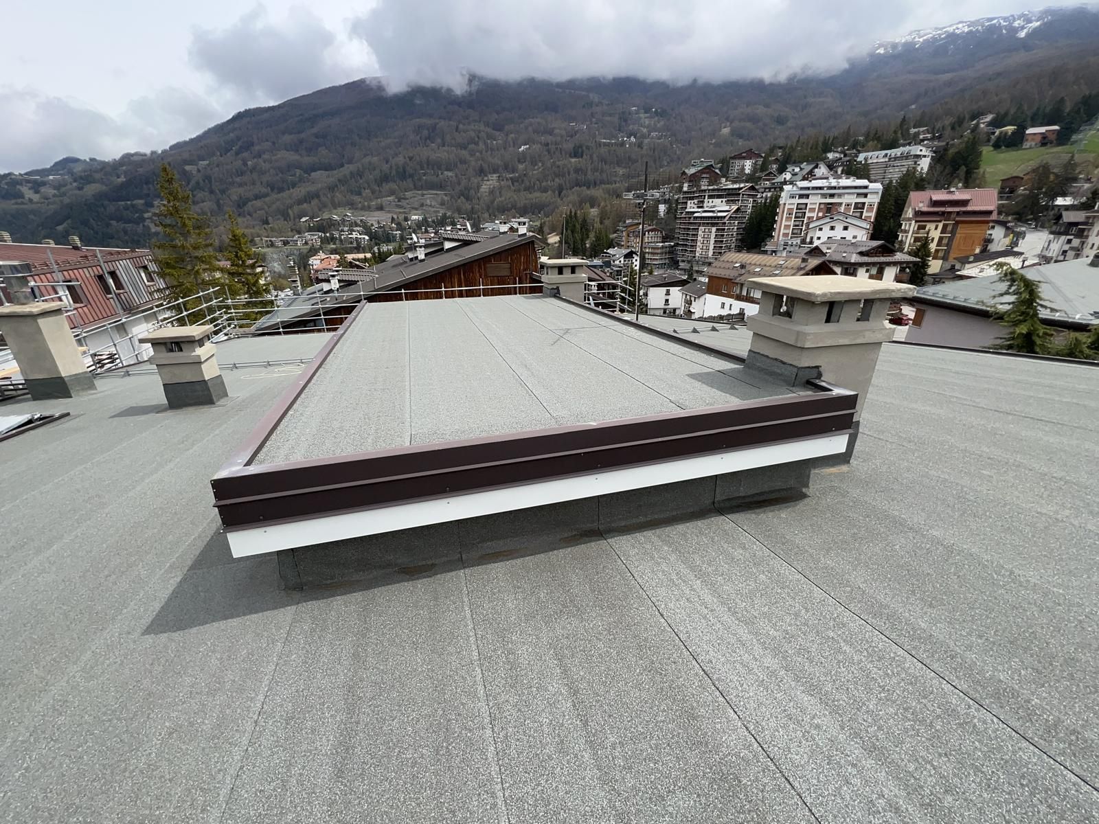 Terrazza sul tetto con lucernario centrale, affacciata su una cittadina di montagna sotto un cielo nuvoloso.