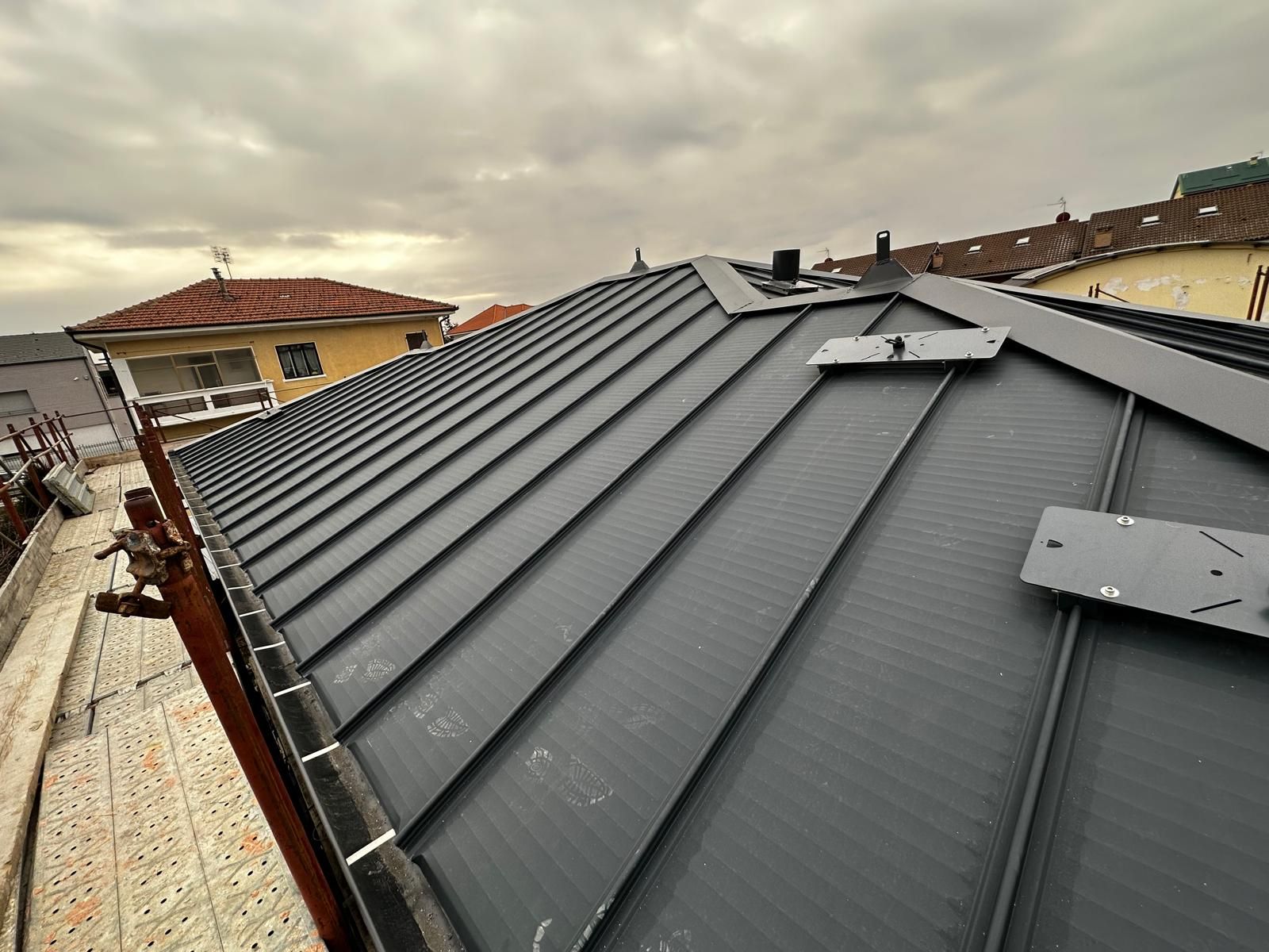 Tetto in metallo nero con prese d'aria su un edificio residenziale sotto un cielo nuvoloso.