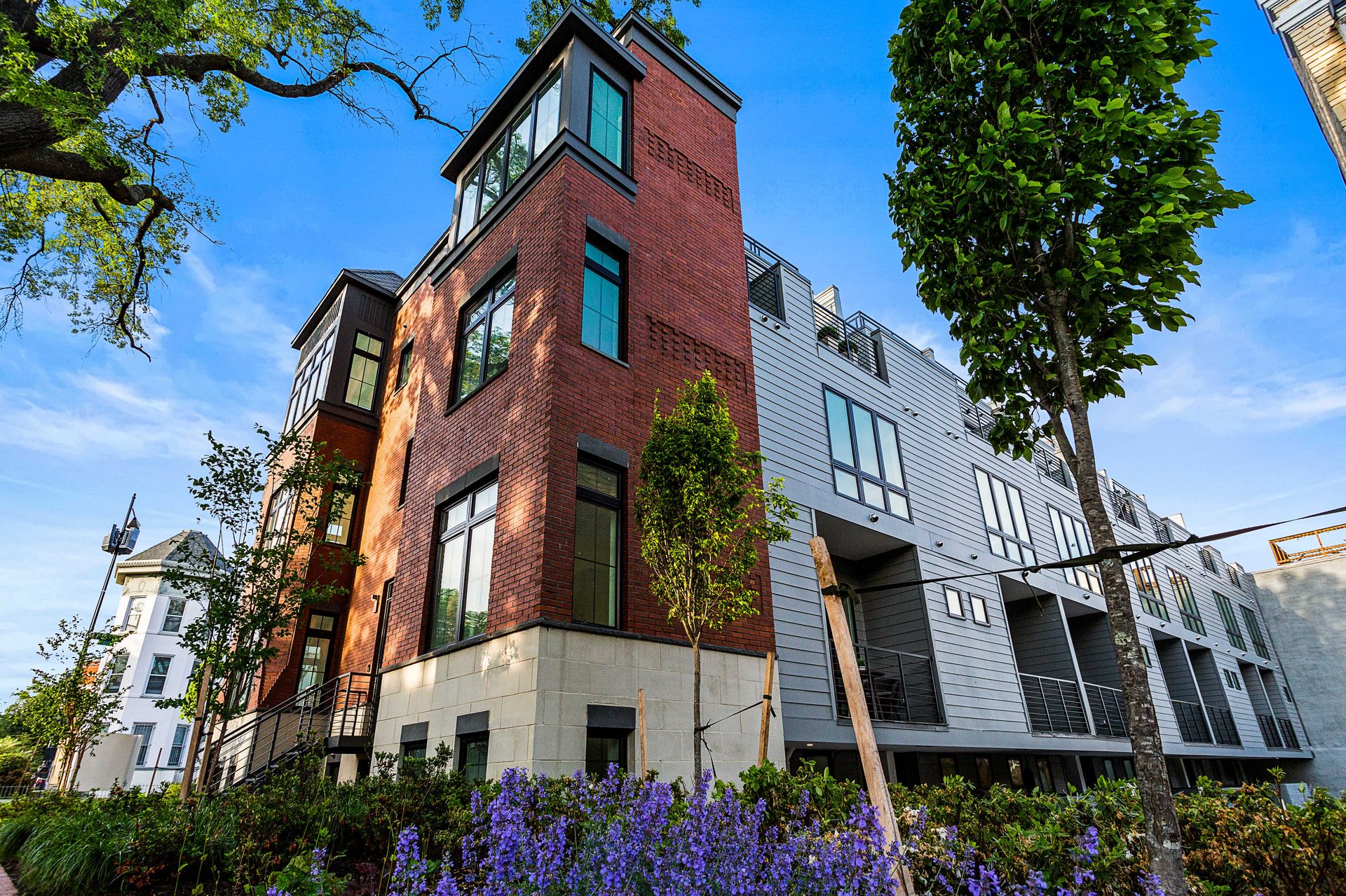 A large brick building with a lot of windows is surrounded by trees and flowers.