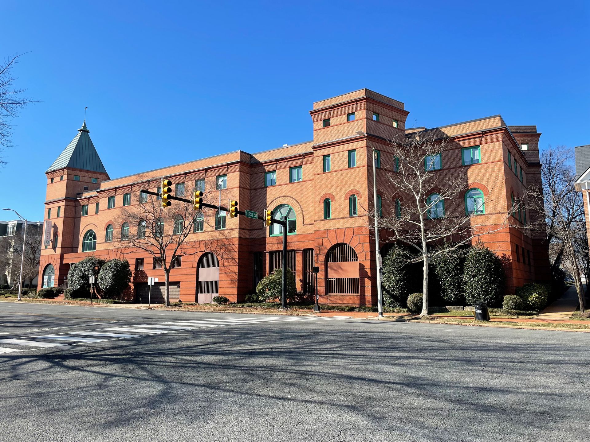 A large brick building with a tower on top of it is sitting on the corner of a street.