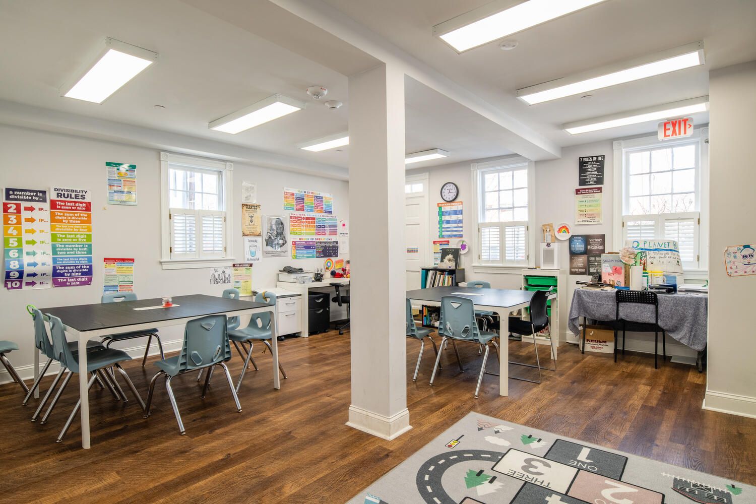 A large classroom with wooden floors , tables and chairs.