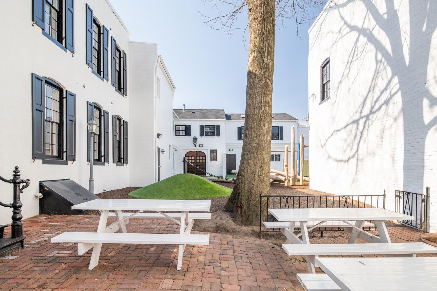 A group of white picnic tables are sitting on a brick patio in front of a white building.