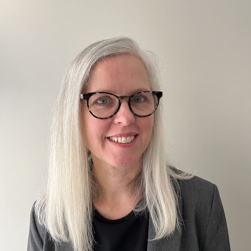 A woman with long white hair and glasses is smiling for the camera.