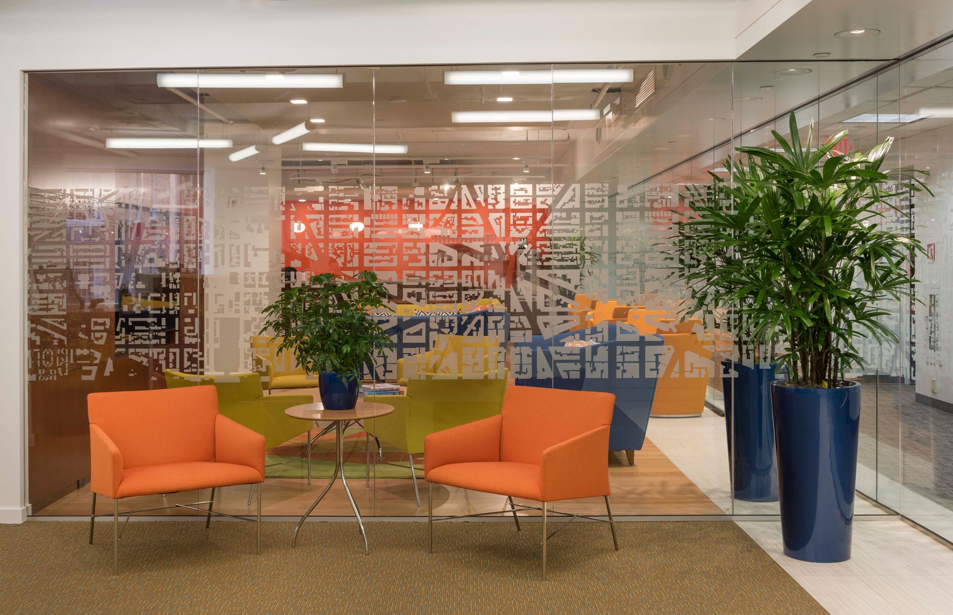 A waiting room with orange chairs and potted plants in front of a glass wall.