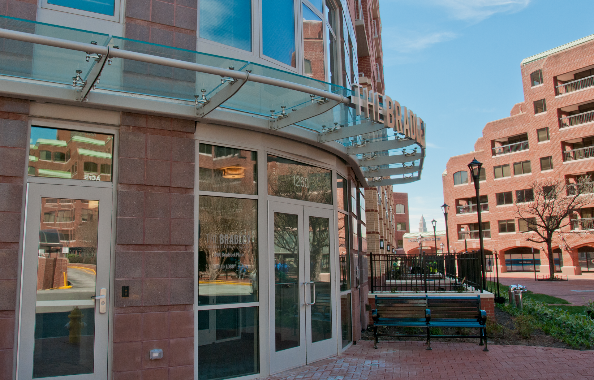 A building with a glass canopy over the entrance and a bench in front of it.