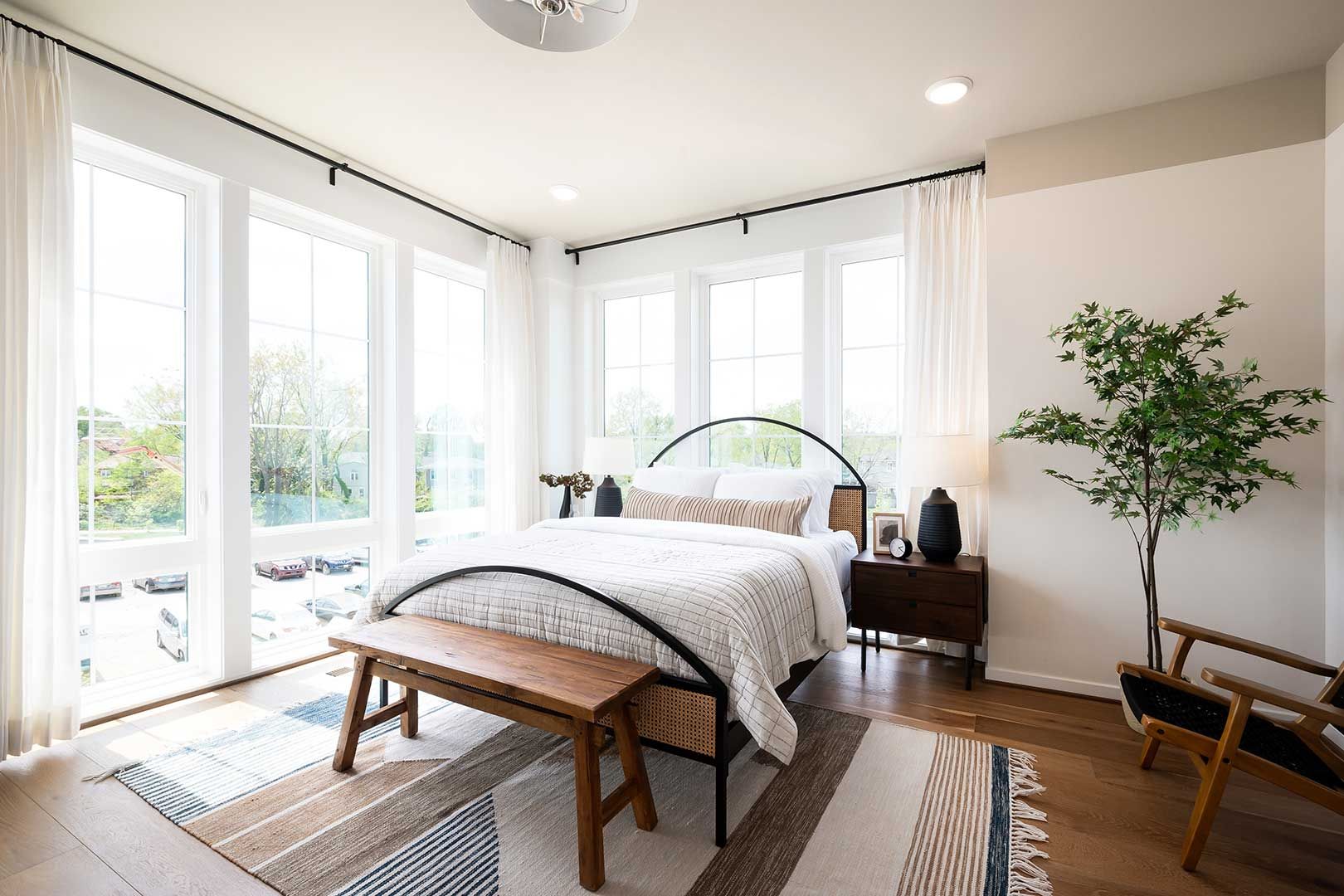 A bedroom with a bed , bench , chair and lots of windows.