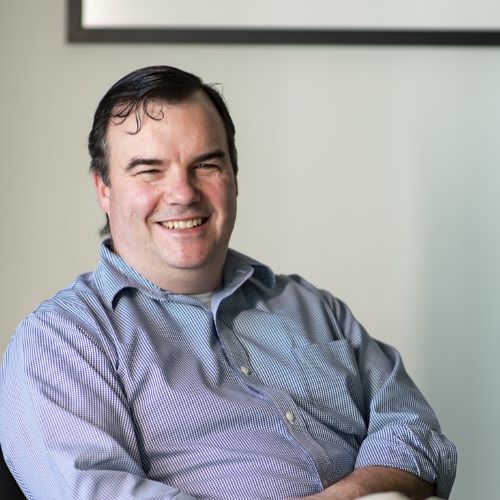 A man in a blue and white striped shirt is smiling while sitting in a chair.