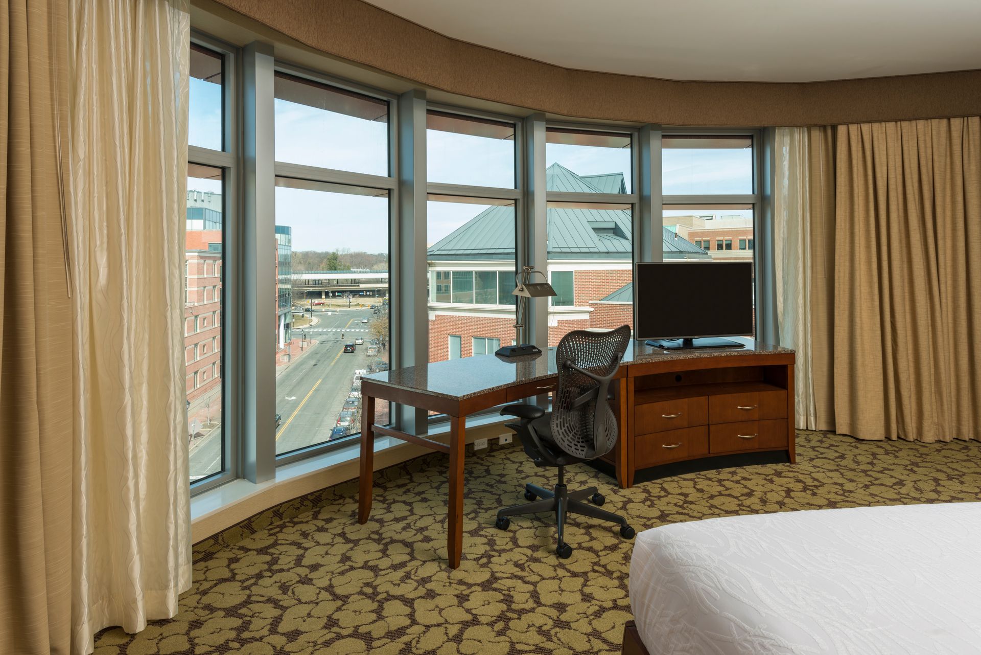 A hotel room with a king size bed , desk , chair and large windows.