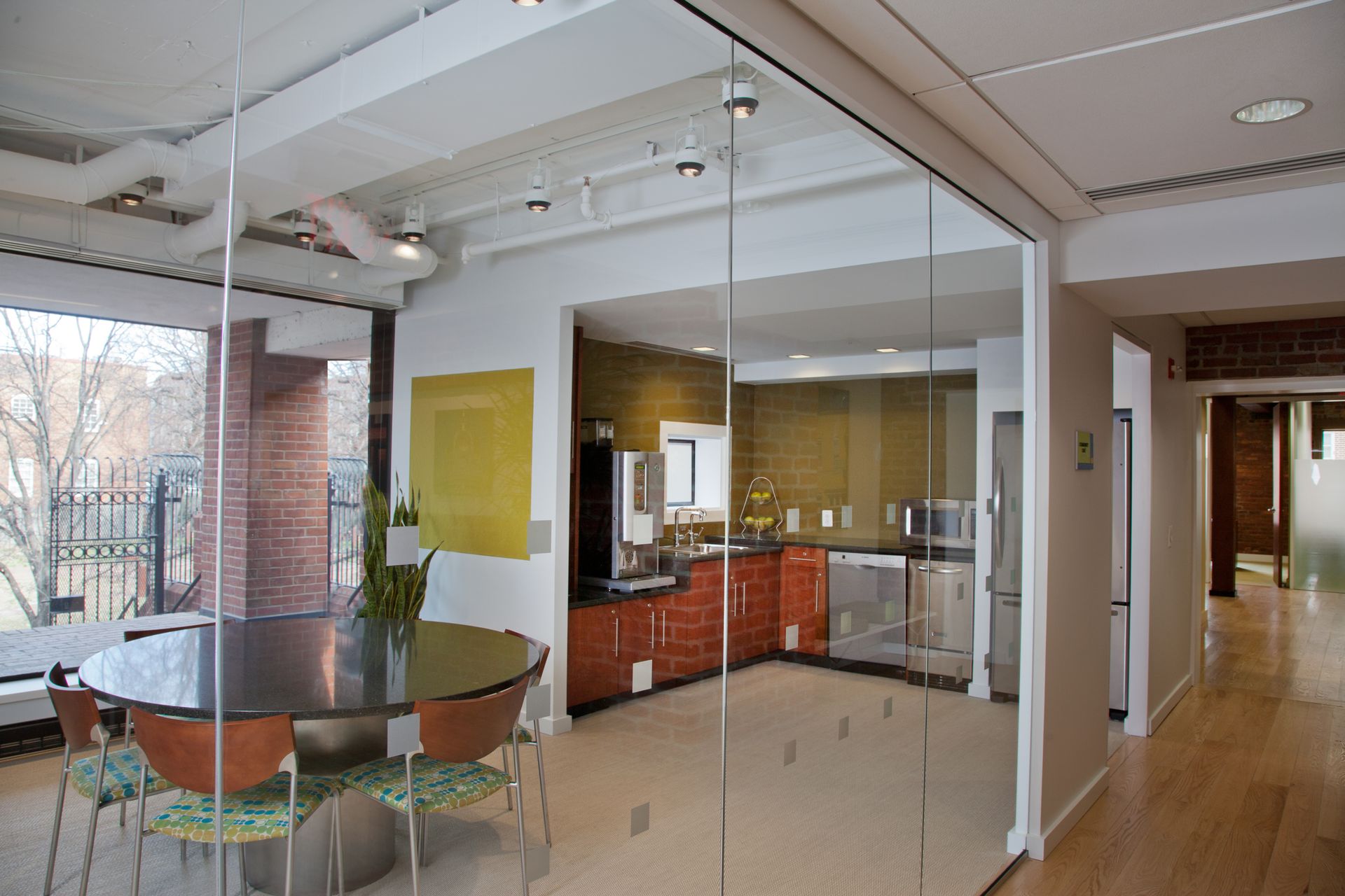 A glass wall separates a dining room from a kitchen