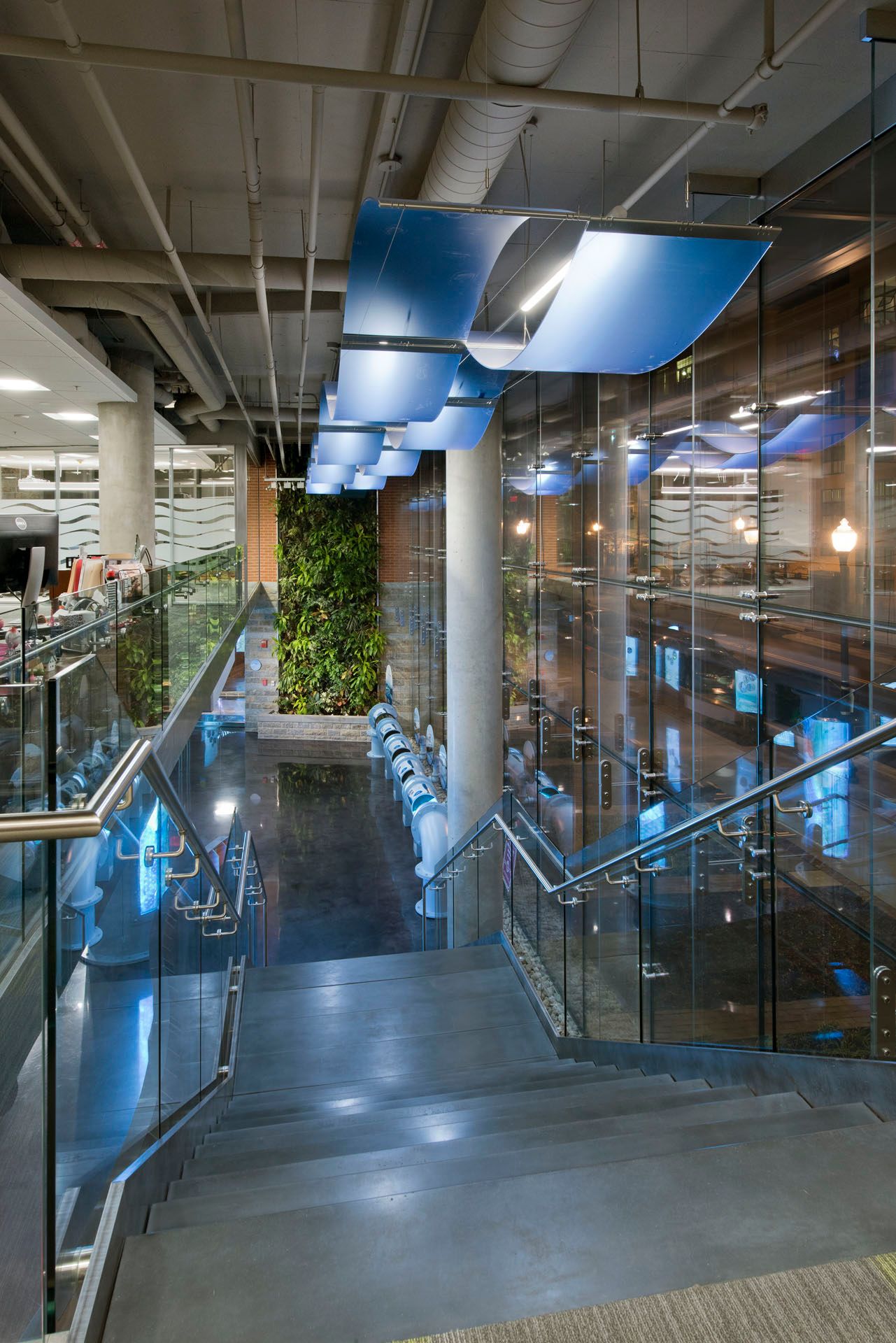 A staircase in a building with a glass railing and a green wall.