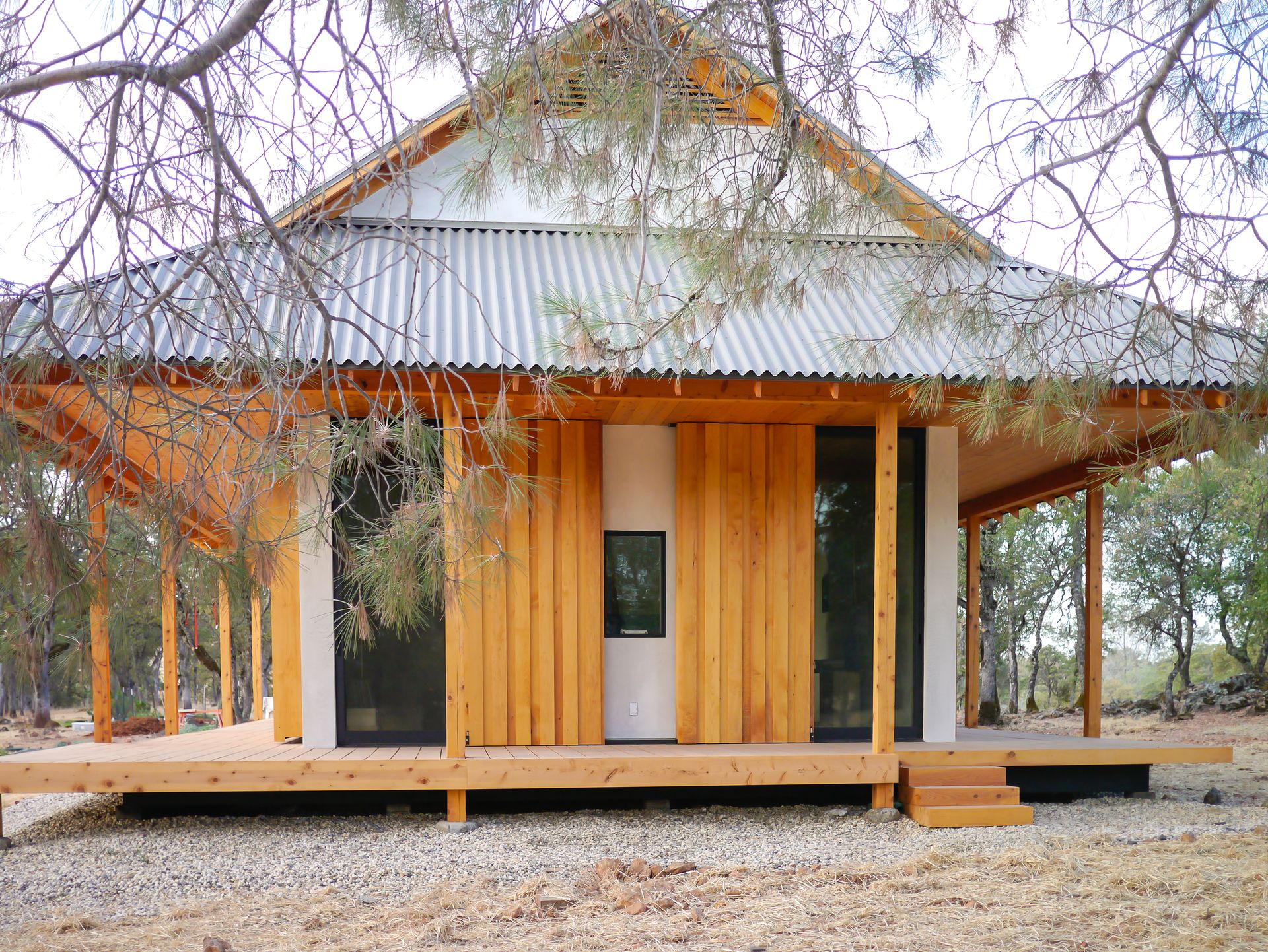 A small wooden house with a metal roof and a porch surrounded by trees.