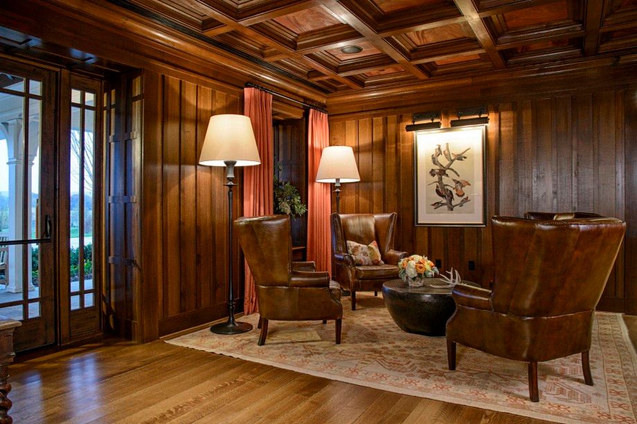 A living room with wood paneling , chairs , lamps and a table.