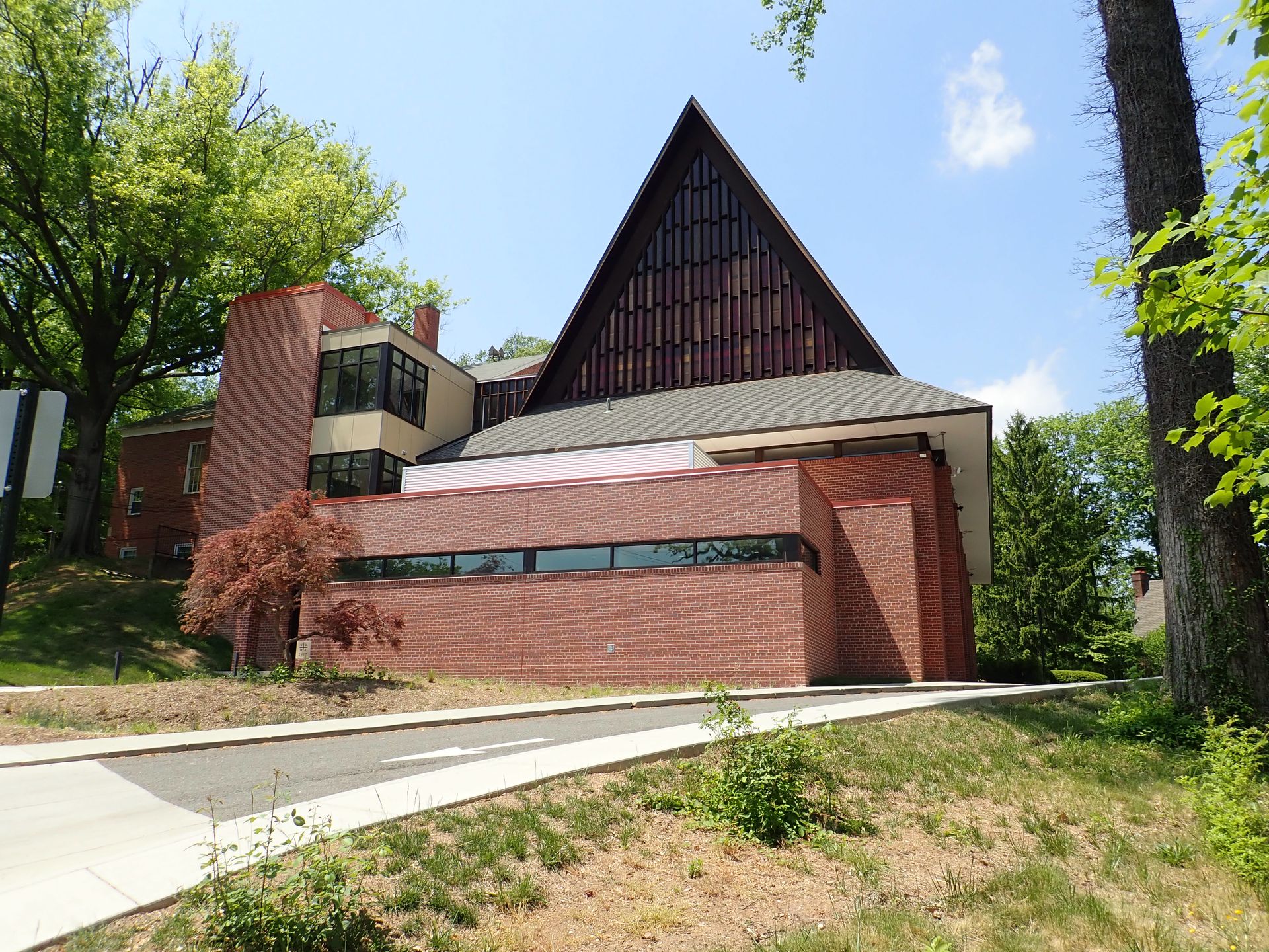 A large brick building with a triangle shaped roof is surrounded by trees.