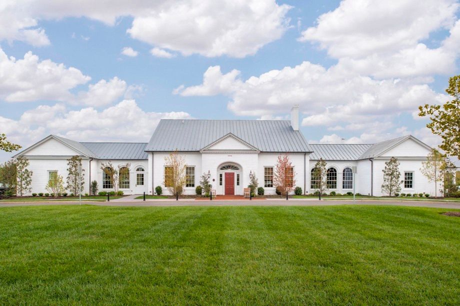 A large white house with a gray roof is sitting on top of a lush green field.