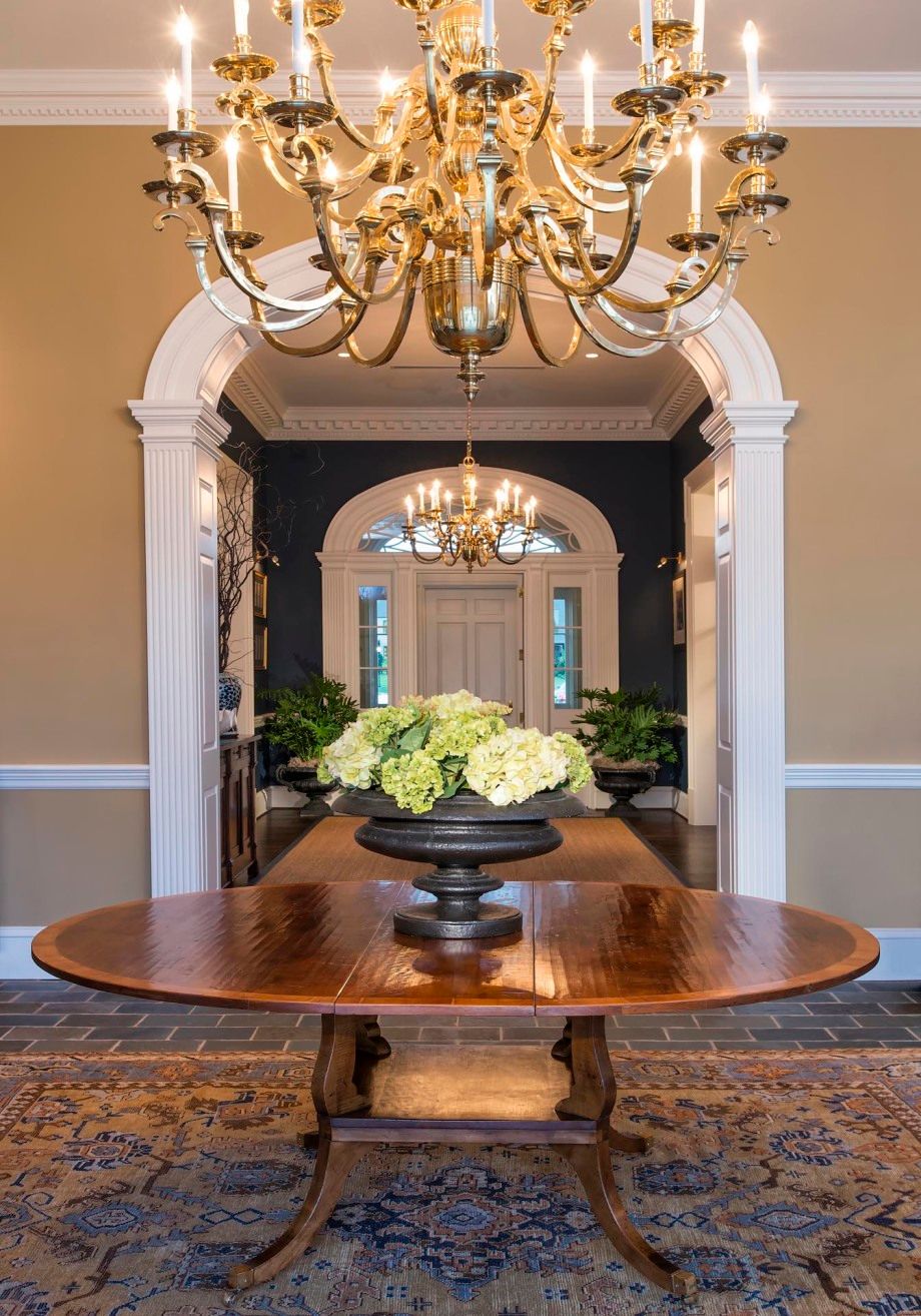 A table with a vase of flowers on it in a hallway with a chandelier.