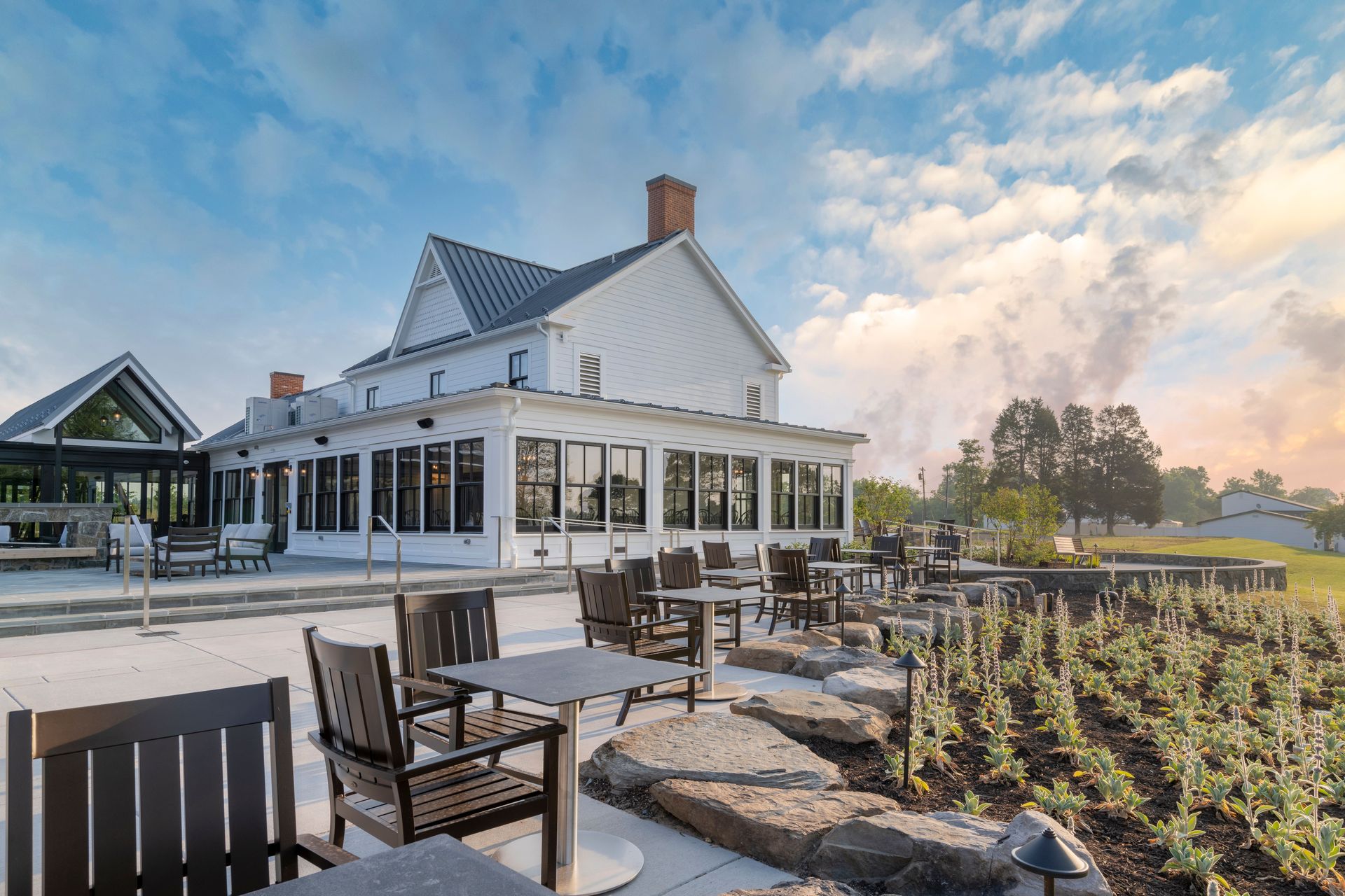 A large white house with tables and chairs in front of it.