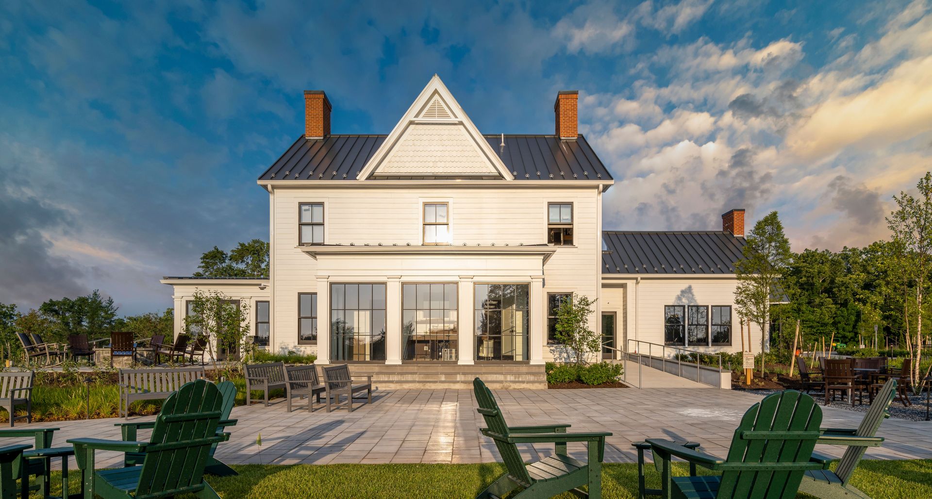 A large white house with a black roof and green chairs in front of it.