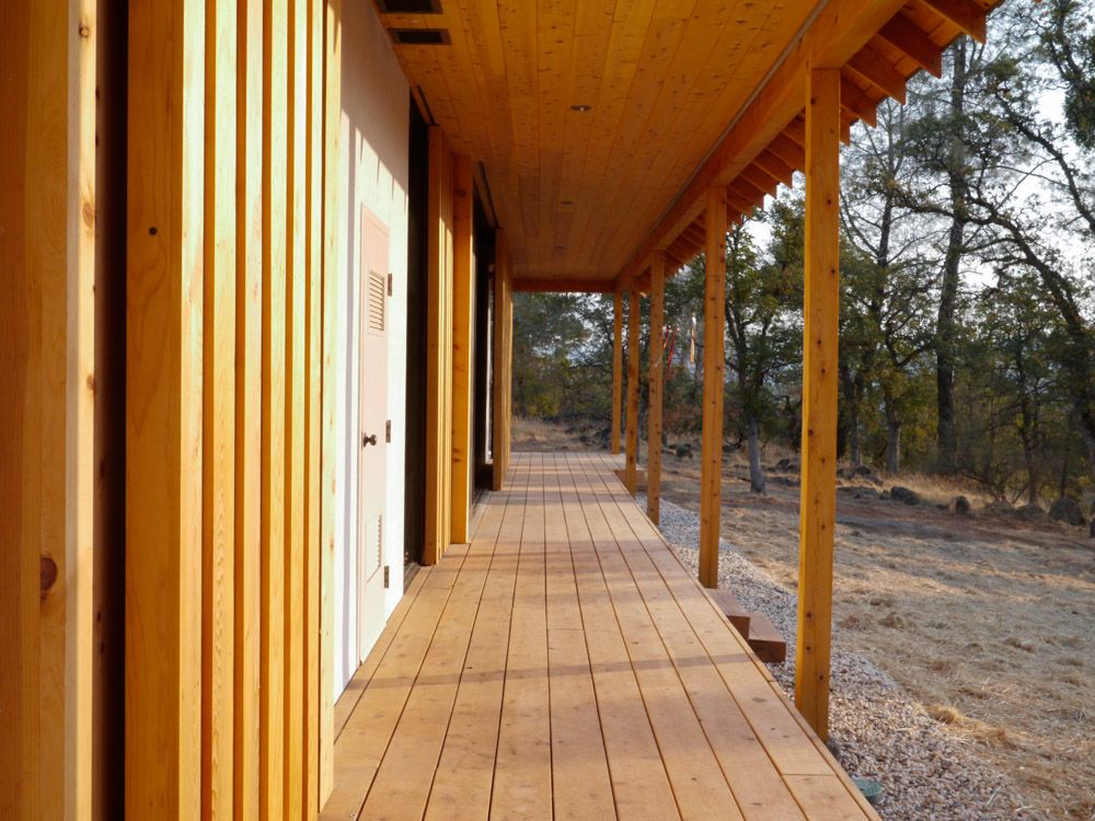 A long wooden porch leading to a house with trees in the background.