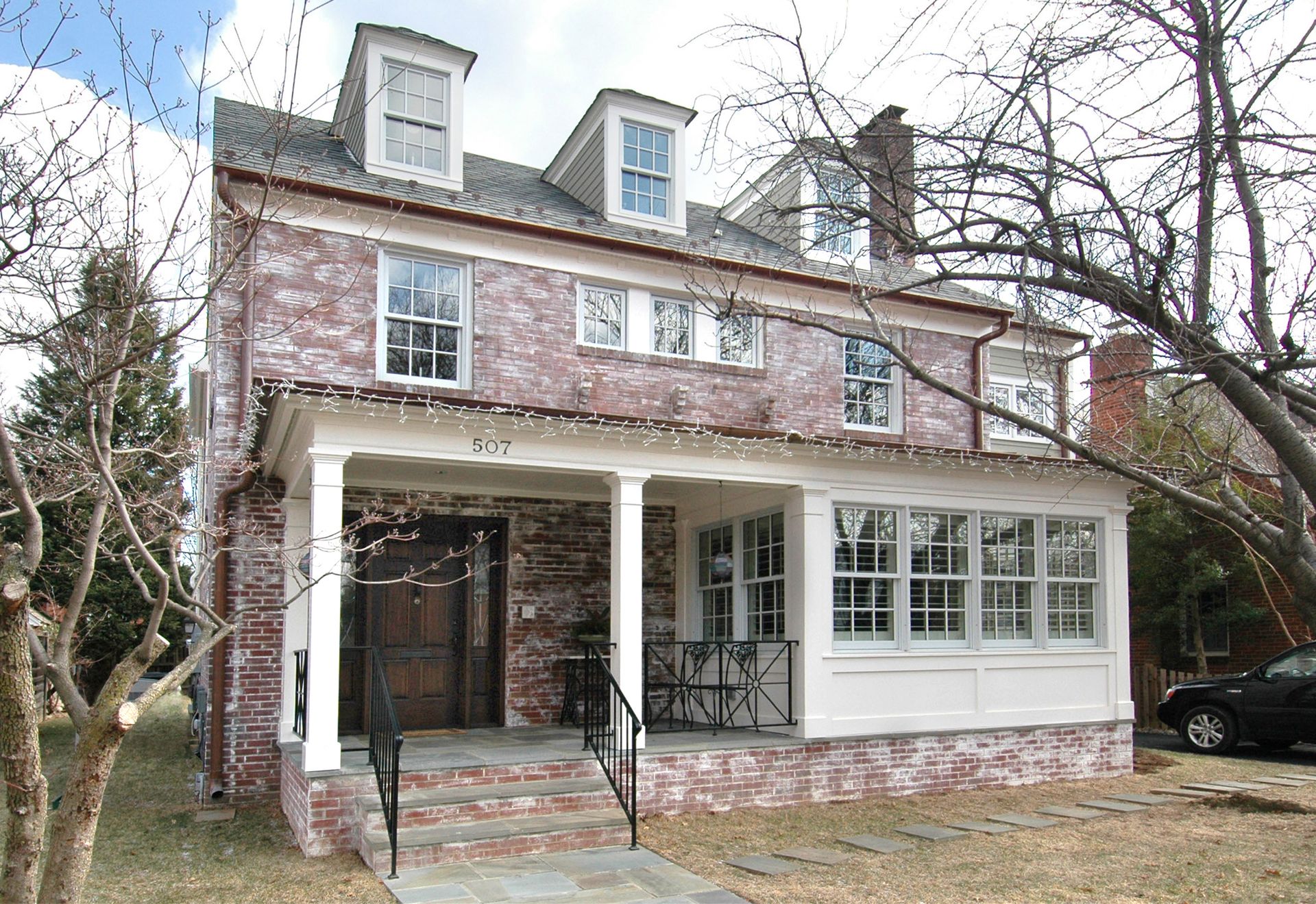 A large brick house with a porch and a car parked in front of it