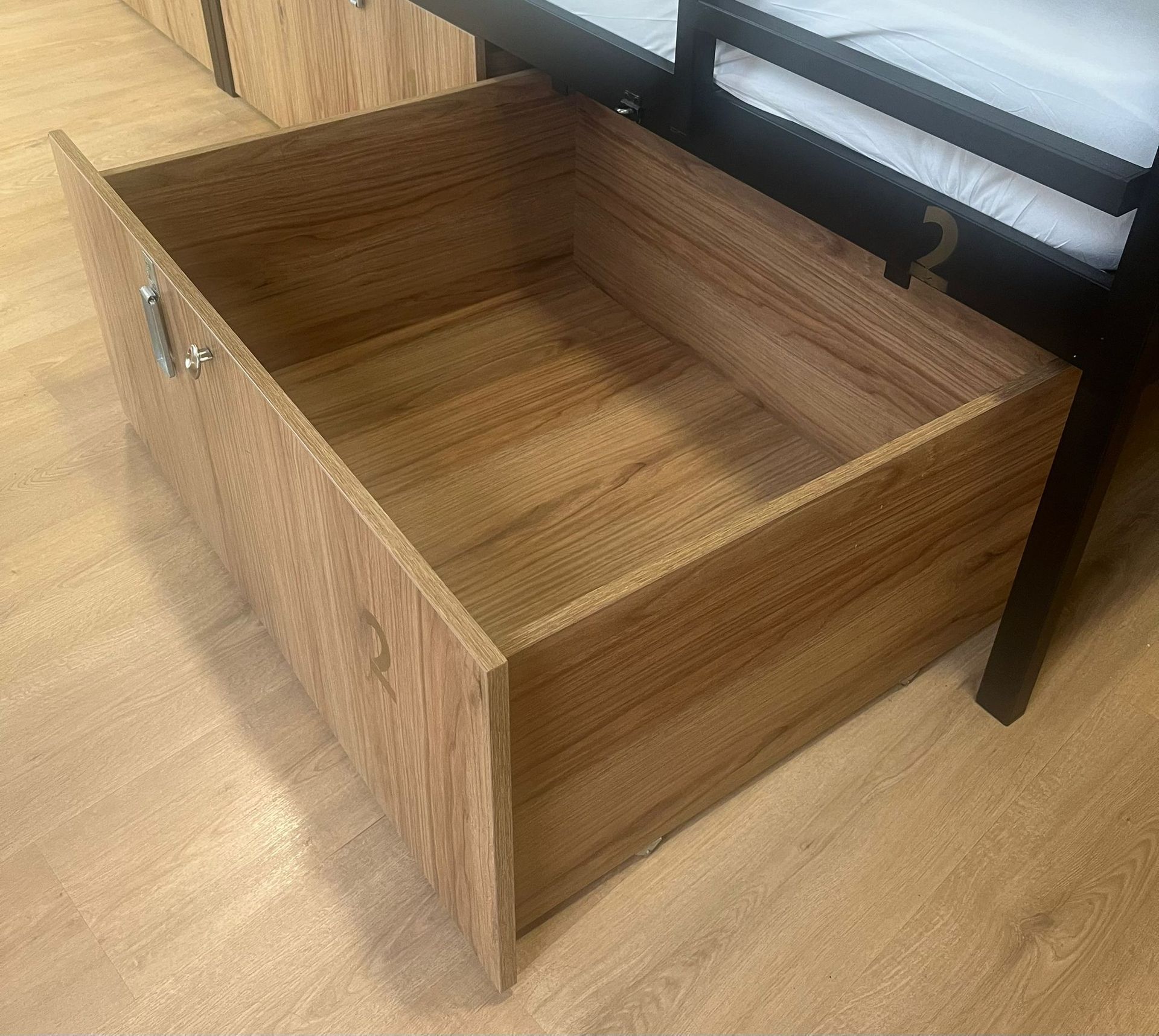 Cajón de madera abierto debajo de una litera, visto desde arriba.