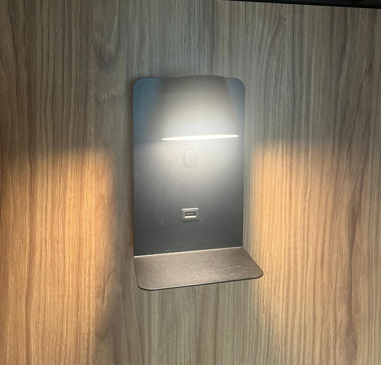 Cargador inalámbrico negro sobre superficie de madera, iluminado con luz blanca.