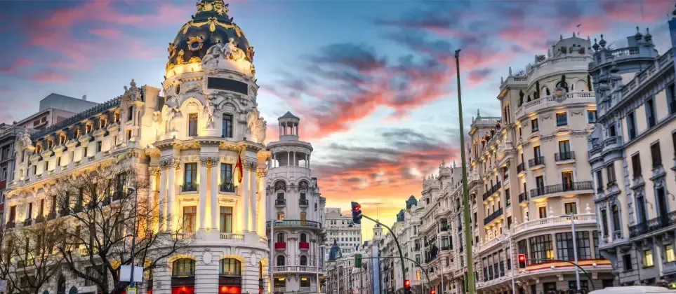 Edificios a lo largo de una calle de Madrid, España, iluminados al atardecer con un cielo colorido.