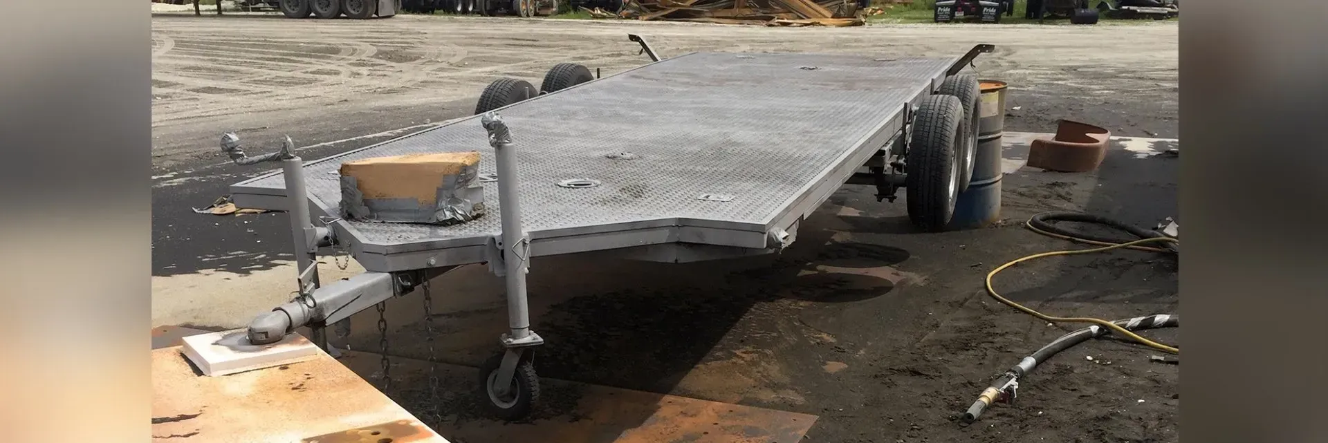 Flatbed trailer carrying a large gray slab outdoors on a dirt lot, with tools and buckets nearby