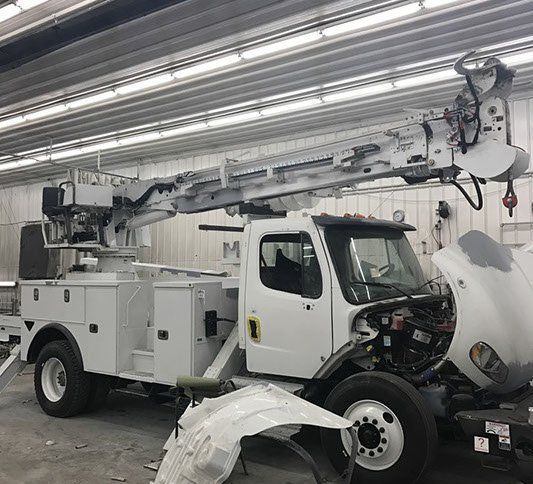 Damaged white utility truck with boom arm inside a garage, front end torn apart.