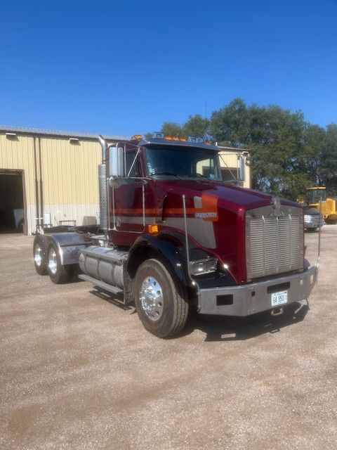 Red semi-truck parked outside a beige industrial building under a clear blue sky