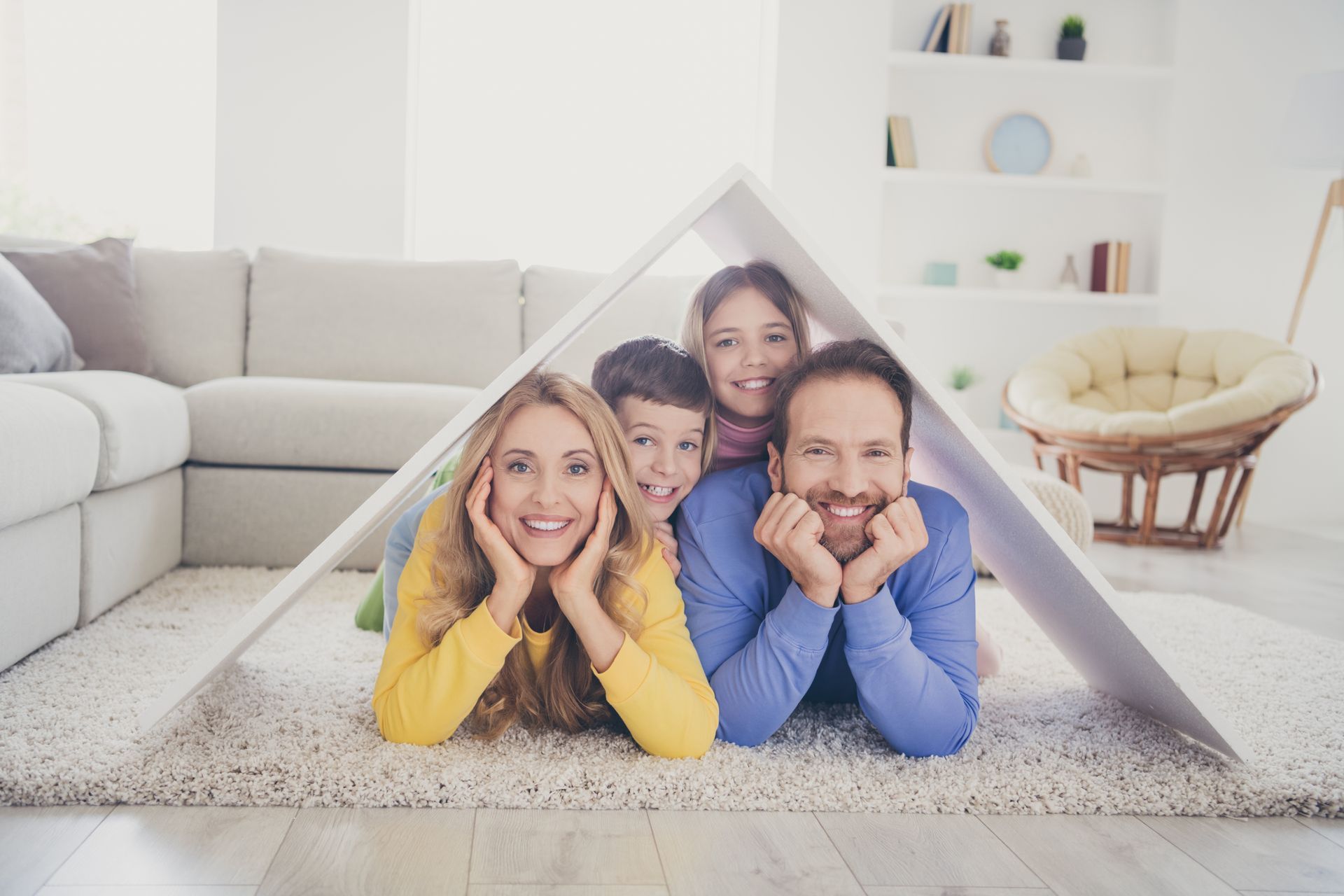 Three people smiling inside a blanket fort in a bright living room