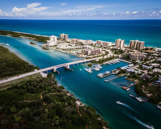Aerial view of a coastal resort city with turquoise water, a bridge, marina, and ocean in the background