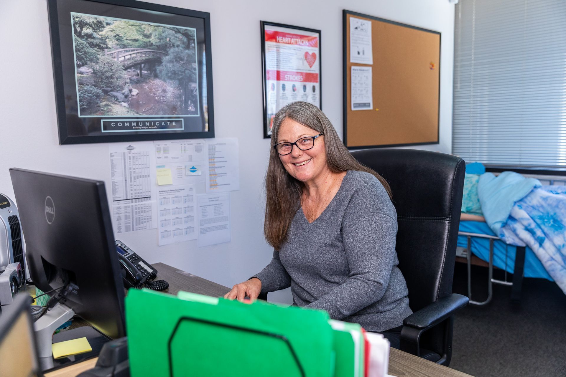 Woman smiling at desk in an office, with computer, corkboard, and framed wall art.