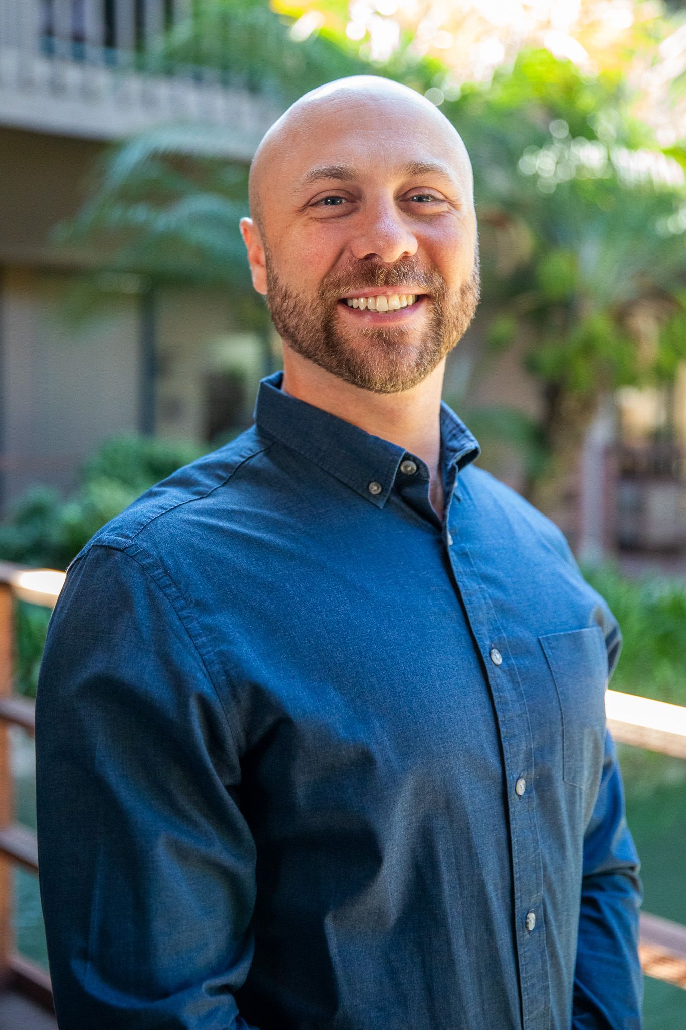 A bald man with a beard is standing with his arms crossed and smiling.