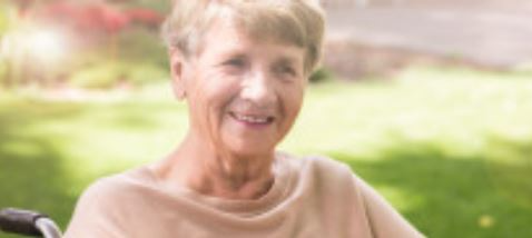 An elderly woman is sitting in a wheelchair and smiling.